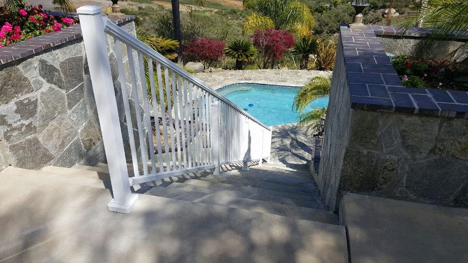 White aluminum handrail with three-quarter-inch square pickets above a stone pool wall