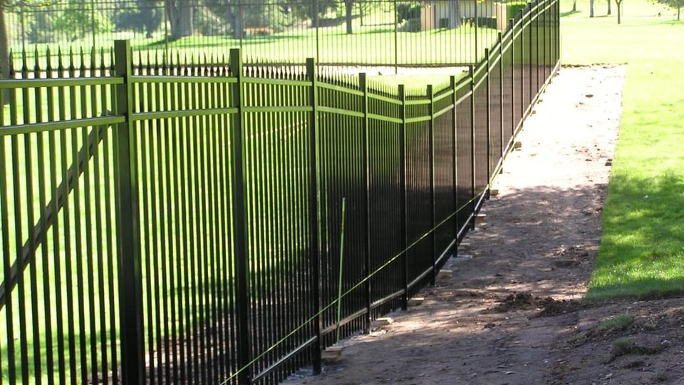 Black iron fence following the contour of a green slope