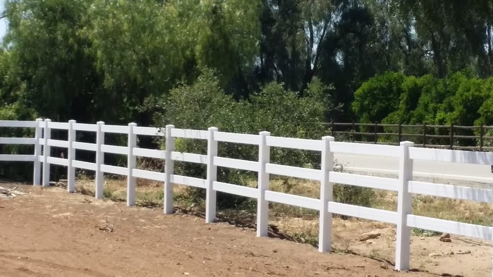 White three-rail ranch fence running along a graded rural property in Valley Center