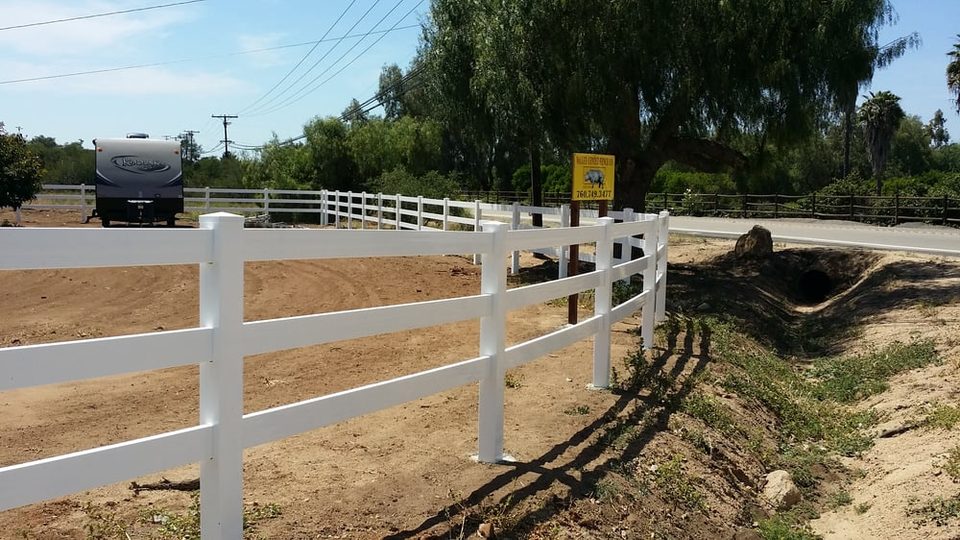White three-rail ranch fence along a rural driveway with an RV parked beyond
